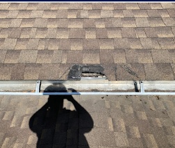 Damaged shingles and exposed decking along a roof edge before repair
